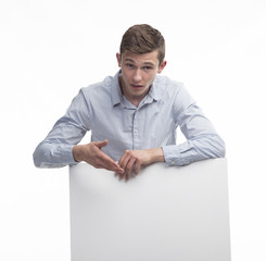 Young surprised man portrait of a confident businessman showing presentation, pointing paper placard gray background. Ideal for banners, registration forms, presentation, landings, presenting concept.