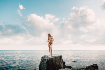 Wall Mural - Young sexy woman in bikini swimsuit on stone and sea with sky, tropical island, summer vacation