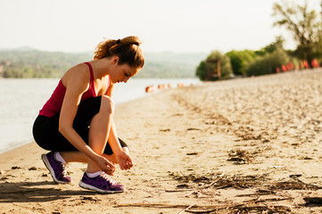 Attractive woman tying a shoe lace while running on the beach.