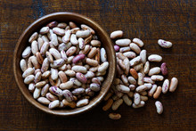 Dry Pinto Beans In Dark Wooden Bowl Isolated On Dark Brown Wood From Above. Spilled Beans.