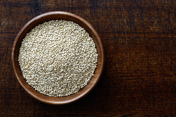 Quinoa seeds in dark wooden bowl isolated on dark brown wood from above.