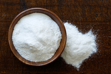 Wall Mural - White rice flour in dark wooden bowl isolated on dark brown wood from above. Spilled flour.