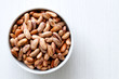 Dry pinto beans in white ceramic bowl isolated on painted white wood from above.