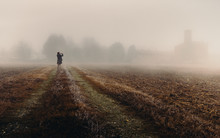 Unidentifable Woman In The Distance Looking At A Church In The Dense Fog Of The Lombardy Region Of Italy During The Winter, Frozen Corn Field