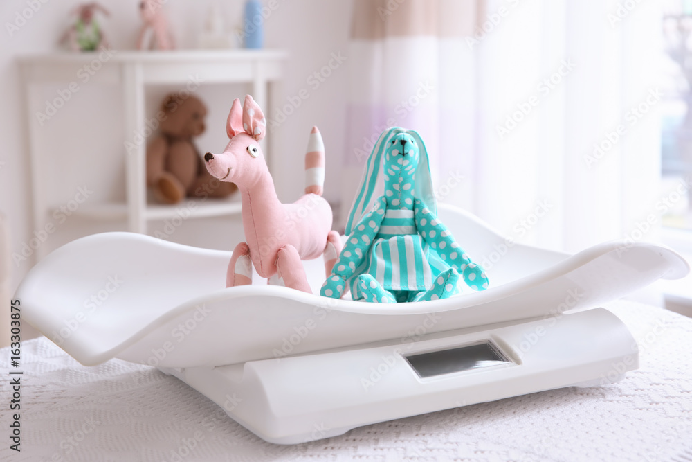 Baby scales with toys on table in light room