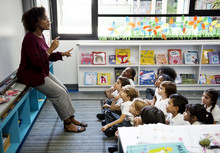 Kindergarten Students Sitting On The Floor Listening To Teacher