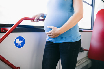 Beautiful young pregnant woman standing in city bus. 