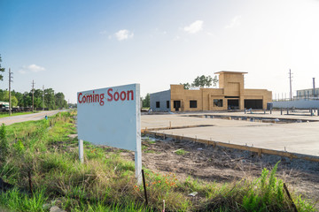 Coming Soon sign stands at the street corner/intersection, under construction convenience store is in background. Signboard with the words Coming Soon outdoor for brand new gas station soon open.