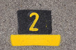 © Gwoeii - Yellow imprint of the number two on an asphalt pavement.