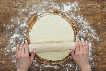 Cropped shot of female hands rolling pizza dough with rolling pin