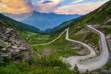 Dirt Mountain Road Leading To High Mountain Pass In Italy (Colle Delle Finestre). Expasive View At Sunset, Colorful Dramatic Sky, Adventures In Summer Time, Italian Alps.