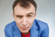 © Евгений Вдовин - Young man looks sullenly with a narrowed eye. A man in a blue jacket and a red T-shirt. Frowns with wrinkles. Close-up close view.