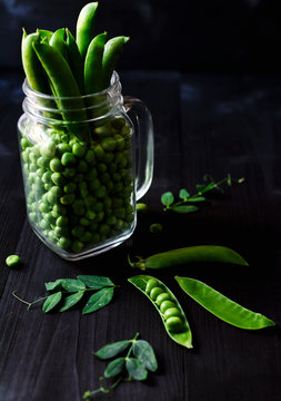 full glass jar with fresh green peas and pods on black wooden background. bio healthy food. green pe