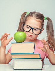 Wall Mural - beautiful cute little girl looking at green apple on thick books