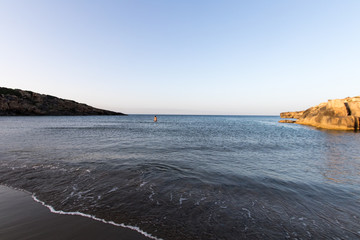 Calm sea beach and rocks a woman alone in the distance is going to swim