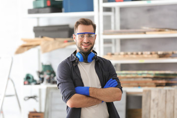 Canvas Print - Young smiling carpenter standing with crossed hands in workshop