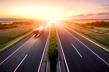 Wall Mural - Highway landscape in a strong back light at sunset with motion blurred truck