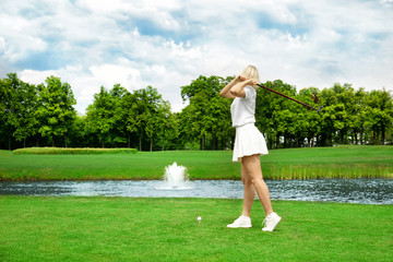 Wall Mural - Beautiful young woman playing golf on course in summer day