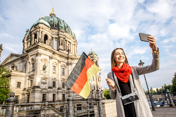 Wall Mural - Young woman tourist making selfie with german flag in front of the famous cathedral in Berlin city