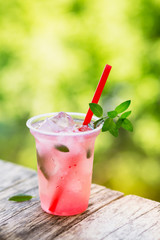 Wall Mural - Refreshing berry drink with ice and mint on an outdoor wooden picnic table.