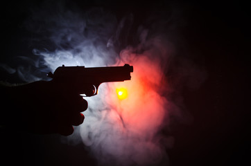 Male hand holding gun on black background with smoke ( yellow orange red white ) colored back lights, Mafia killer concept