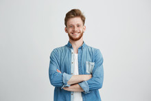 Portrait Of Young Handsome Man In Jean Shirt Smiling Looking At Camera With Crossed Arms Over White Background.