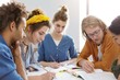 © wayhome.studio  - Five mixed race college students sitting together at table underline important information in books for their project having serious expressions helping each other. People and cooperation concept