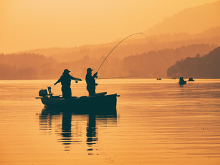 Silhouette of man fishing on lake from boat at sunset. Lake of Menteith, Stirlingshire, Scotland, UK