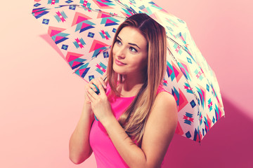 Happy young woman holding an umbrella on a pink background