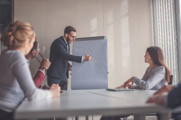 Wall Mural - Confident handsome young businessman giving presentation using flipchart in office