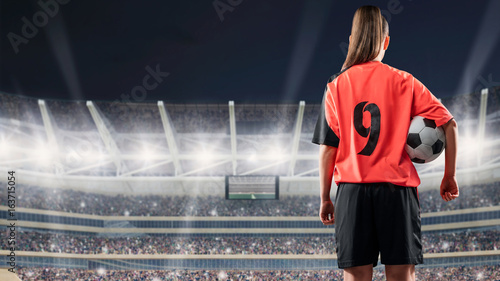 Obraz na płótnie kobieta piłkarz stojący z piłką przeciwko zatłoczonym stadionie w nocy