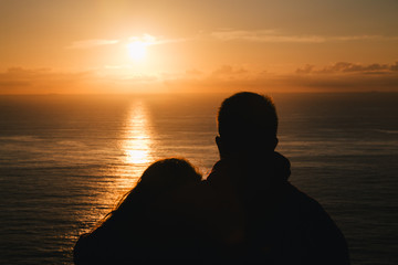 Romantic couple watching the sunset in the ocean. Silhouette