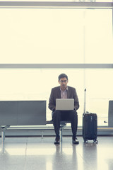 Wall Mural - Asian Indian business man sitting on chair and using laptop while waiting his flight at airport.