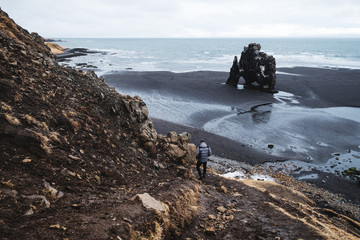 Wall Mural - landscape hvitserkur in iceland, young traveling hiking down from cliff to black sand beach in the m