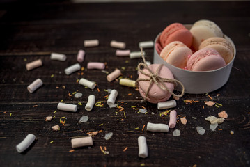 Multi color pastel macaroons in white deep plate decorated with rope on a black wood background