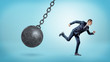 © gearstd - A small businessman running away from a giant black wrecking ball on a chain.
