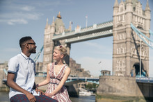 Young Couple Sitting On Wall, Smiling, Tower Bridge In Background, London, England, UK
