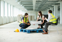 Three People Sitting In Newly Constructed Office Space, Looking At Construction Plans