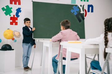 Wall Mural - Schoolboy standing at chalkboard and looking at classmates sitting at desks