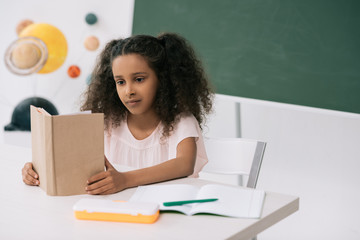 Wall Mural - Concentrated african american schoolgirl reading textbook in class