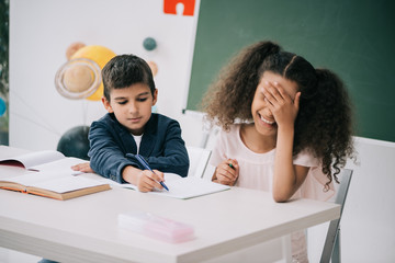 Wall Mural - Schoolboy helping cheerful african american student with exercise at lesson