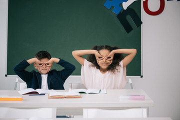 Wall Mural - Cute multiethnic pupils having fun while sitting together at desk in class