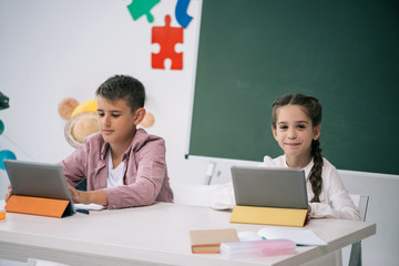 Wall Mural - Cute caucasian schoolkids using digital tablets while studying together in class