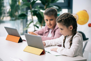 Wall Mural - Cute caucasian schoolkids using digital tablets while studying together in class