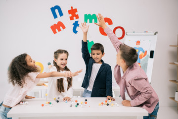 Wall Mural - Multiethnic schoolkids giving high five while studying with molecular model in classroom