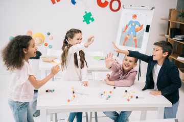 Wall Mural - Multiethnic schoolkids giving high five while studying with molecular model in classroom
