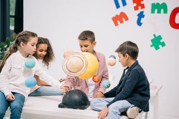 multiethnic group of schoolchildren working with solar system model in classroom
