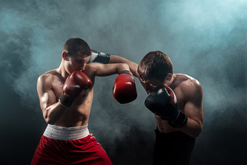 Two professional boxer boxing on black smoky background,