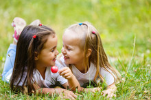Two Little Girls Relaxing And Eating A Lollipop At A Park