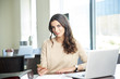 © gzorgz - Working in the office. Shot of a happy young businesswoman sitting at desk in front of laptop and doing some paperwork.